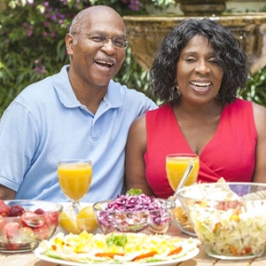 senior man and woman sitting outside at a table with various foods and beverages