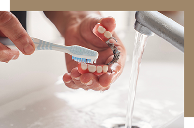 Cleaning a denture in the sink with a toothbrush