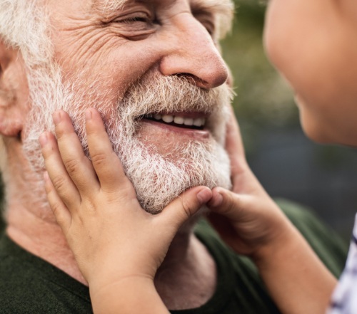 Older man smiling at grandchild after dental implant tooth replacement