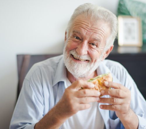 Smiling man with dentures eating a sandwhich