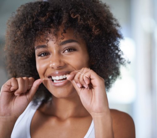 Woman flossing to care for smile after tooth colored filling restoration