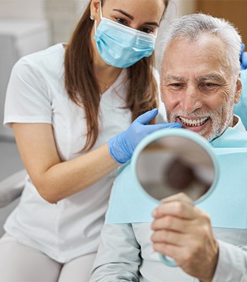 Man with white hair looking into mirror as dentists points to his teeth