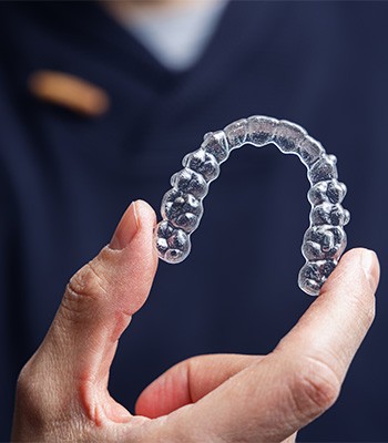 Dentist in dark blue scrubs holding Invisalign with thumb and forefinger