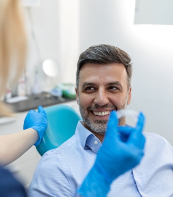 Dentist in dark blue scrubs holding Invisalign with thumb and forefinger
