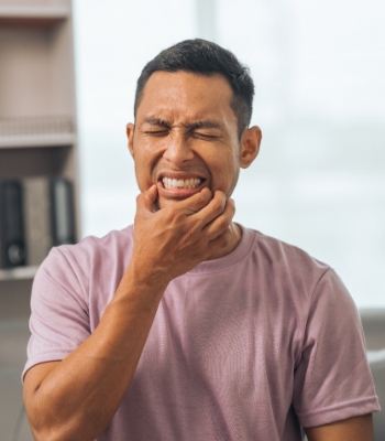 Woman with dark hair in dental chair holding hand to jaw in pain