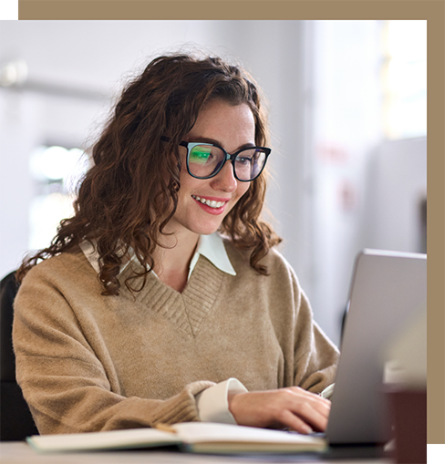 Young woman in glasses and a tan sweater smiling at her laptop