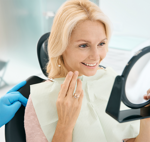 Woman looking at her smile in a mirror after receiving dental services in Cocoa Beach