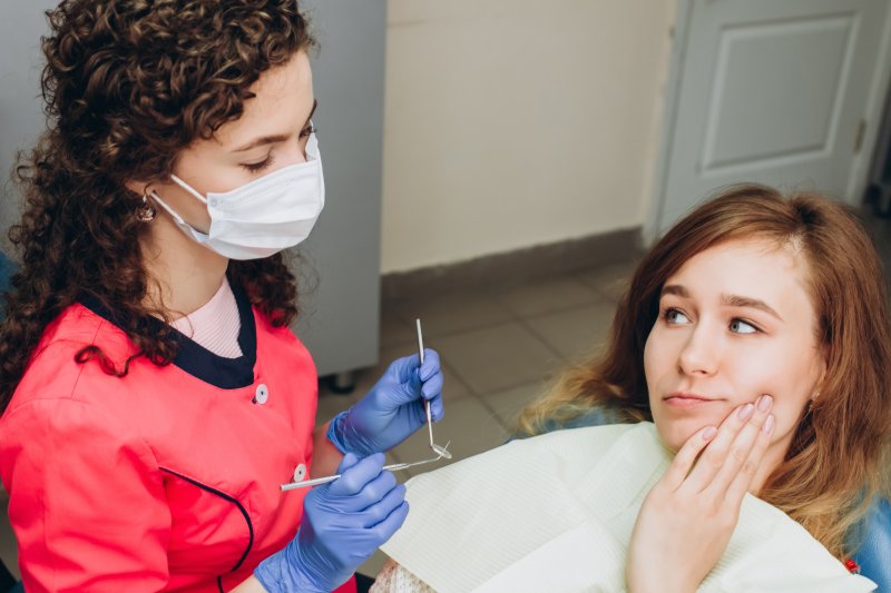 a young female holding her cheek in pain while listening to her dentist