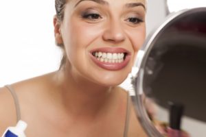 woman looking at her teeth in a mirror to find different types of tooth stains 