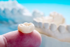 Closeup of a dental crown placed on a finger with a blurry background with dental molds