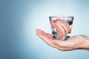 Handing holding a glass of clear liquid with dentures in it