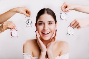 Woman with brown hair smiling surrounded by clocks