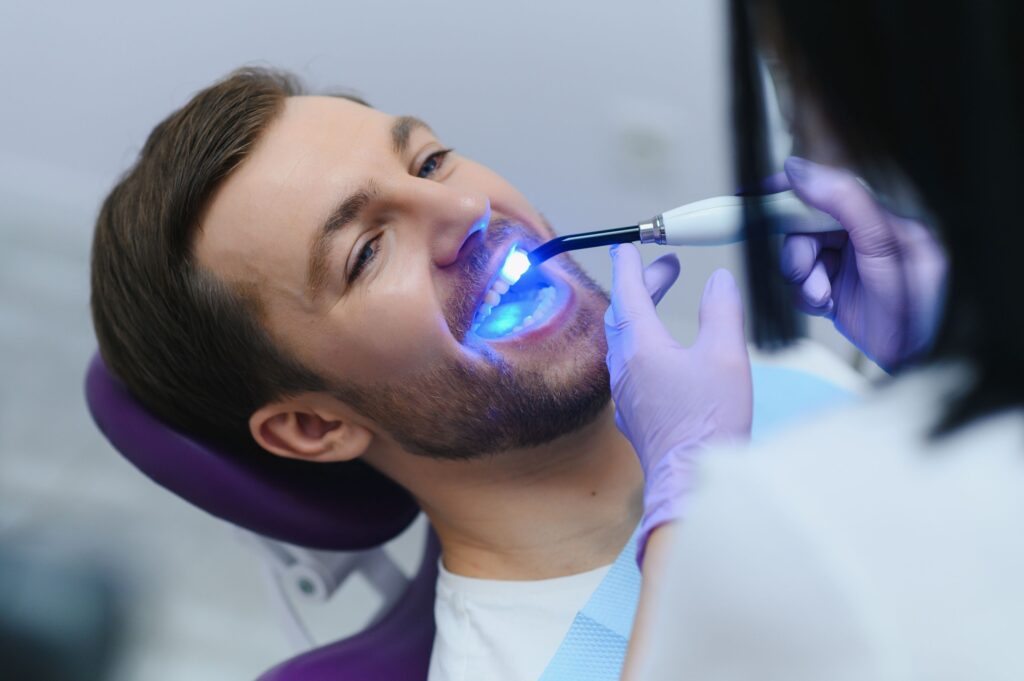 Dentist applying light to harden man's dental filling